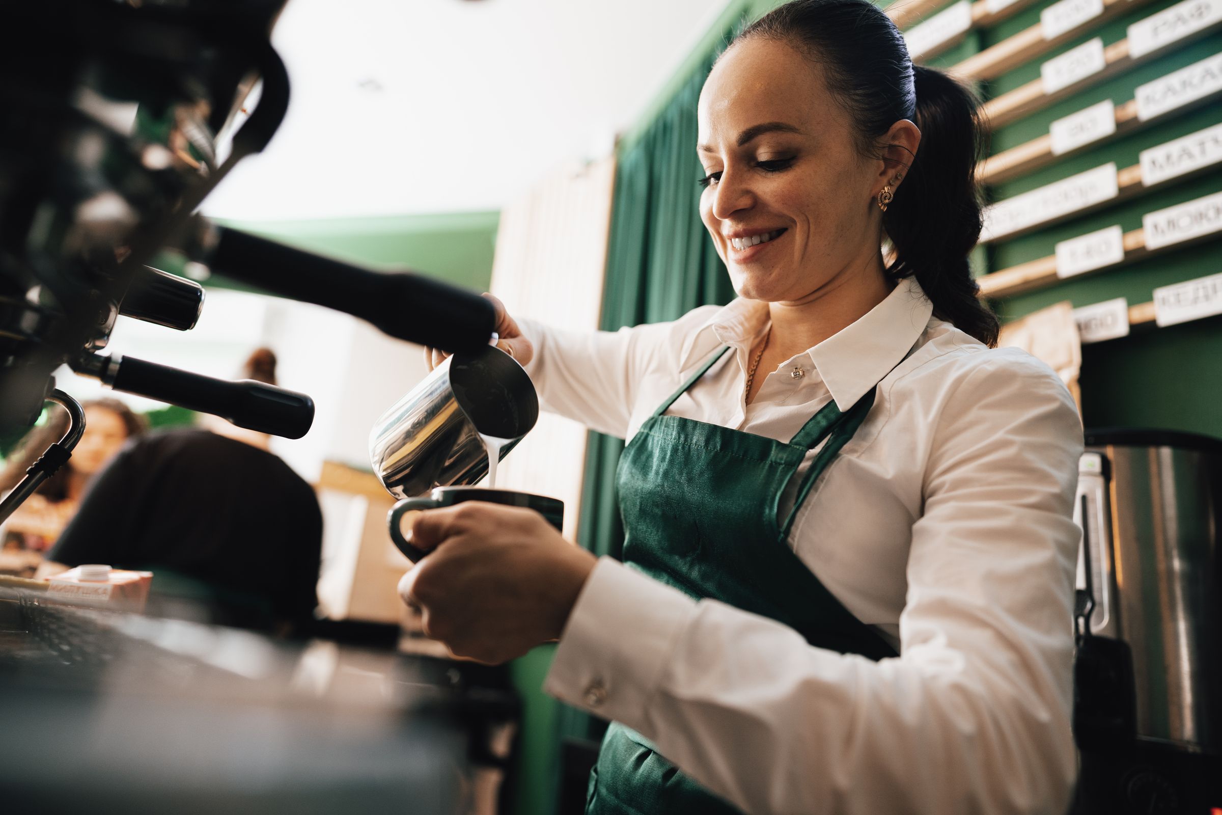 A smiling barista pouring steamed milk into a cup